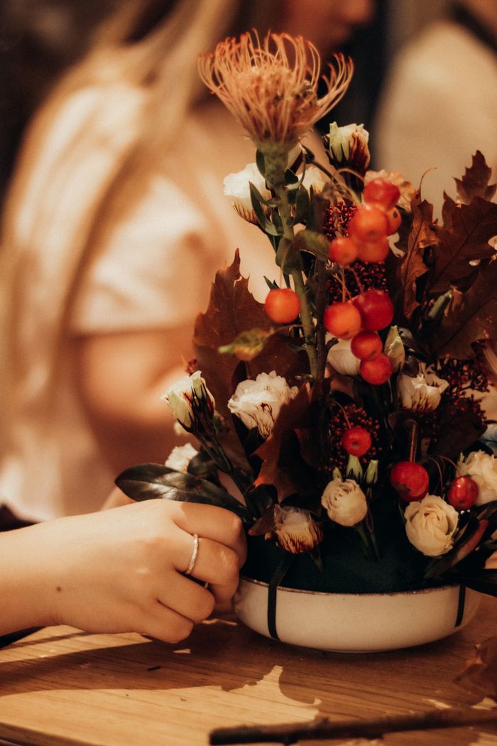 services-04 Warm autumn floral arrangement in a bowl with vibrant orange and red accents, evoking a cozy atmosphere.